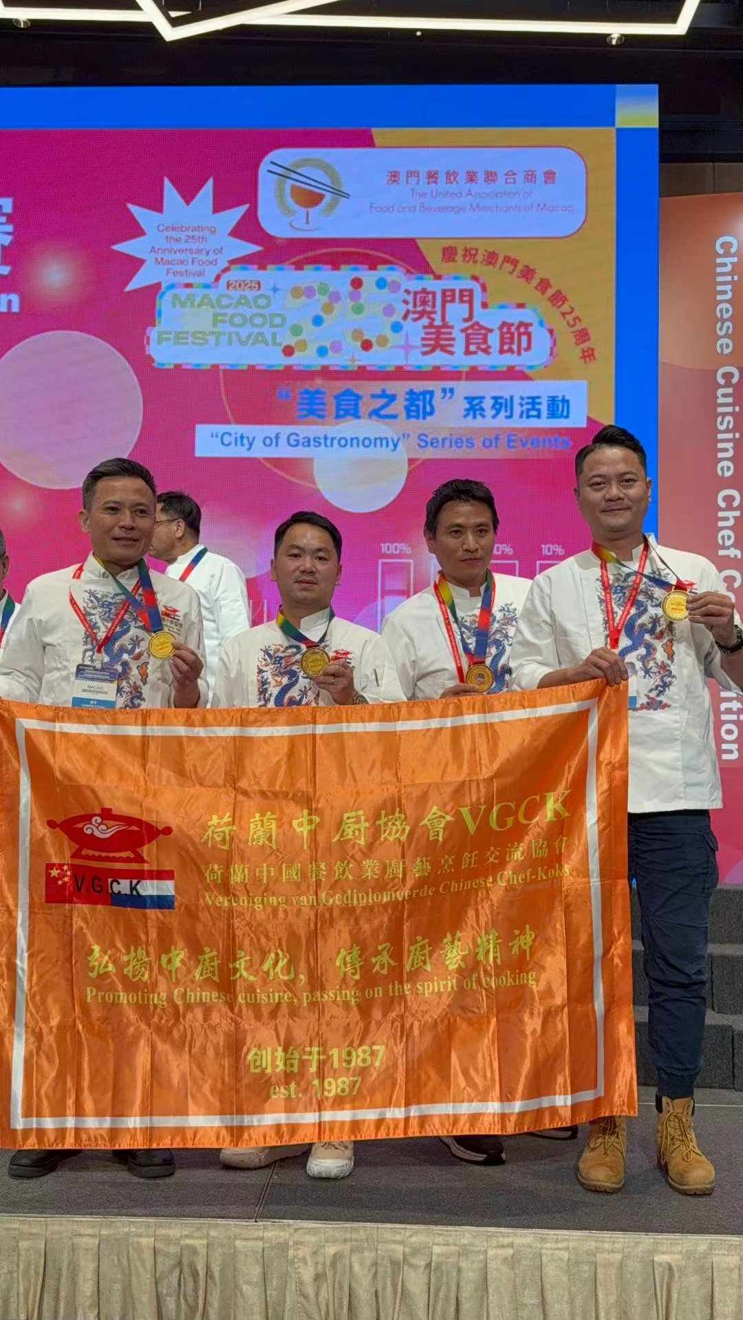 Het Nederlandse team met gouden medailles achter de VGCK-vlag op het podium van het Macao Food Festival