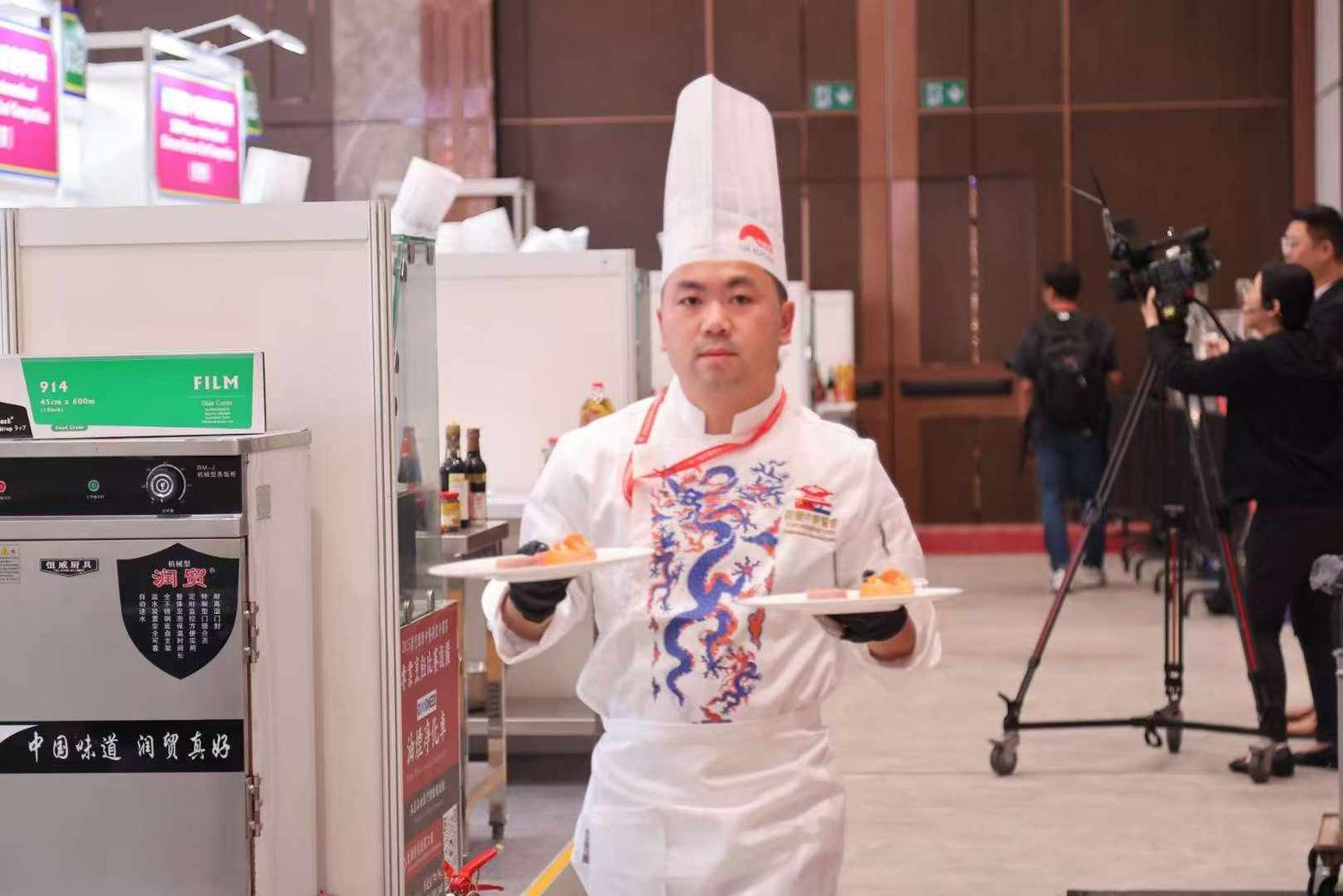 Wang Xing Jian draagt twee opgemaakte borden weg langs de camera’s tijdens de wedstrijd
